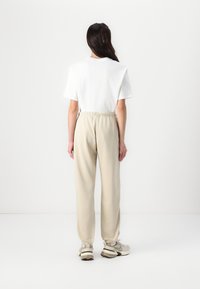 Hvit t-skjorte med rund hals, beige joggebukser med elastisk midje, oppbrettede hem og lysfargede joggesko. Minimalistisk design, myke teksturer.