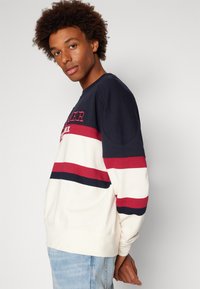 Felpa in cotone con righe orizzontali blu navy, rosse e crema. Presenta collo a giro, polsini a costine e logo ricamato sul petto.