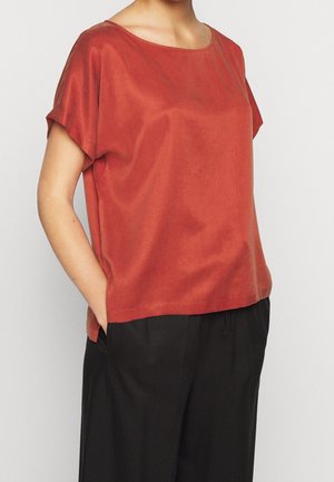 Rostfärgad kortärmad topp med bred halsringning och slät textur. Kombinerad med svarta, löst sittande byxor. Enkelt och minimalistiskt design.