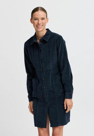 Navy corduroy shirt dress with a collared neckline, button front, pockets, and long sleeves; features a textured fabric and tailored silhouette.