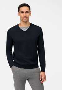 Marineblauwe gebreide trui met een V-hals, lange mouwen, ribbels aan de manchetten en onderkant. Draag het over een grijze shirt, gecombineerd met grijze broek. Soepele textuur.