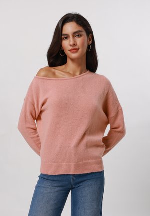 Rosa avskjært genser i mykt strikket materiale, med lange ermer og ribbestrikkede mansjetter, sammen med blå denimjeans.