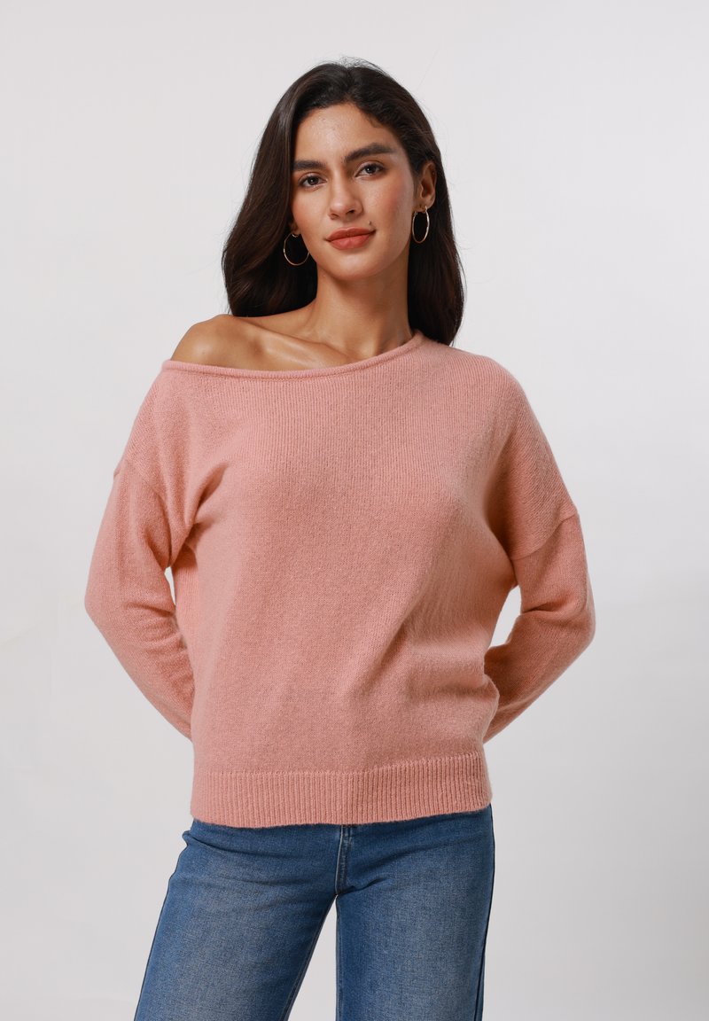Pull rose en maille douce, décolleté épaules nues, avec des manches longues et des poignets côtelés, associé à un jean en denim bleu.