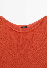 Pull orange en tricot avec un col rond et une étiquette noire cousue à l'intérieur du col avec un texte blanc.