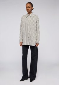 Camicia a righe bianca e nera, con colletto a punta, maniche lunghe e polsini a contrasto, abbinata a pantaloni neri a gamba larga.