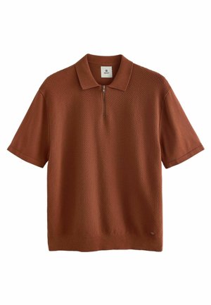Polo à manches courtes de couleur rouille, en tissu tricot texturé. Doté d'une fermeture éclair quart de tour et d'un col classique. Détail du logo subtil à l'ourlet.