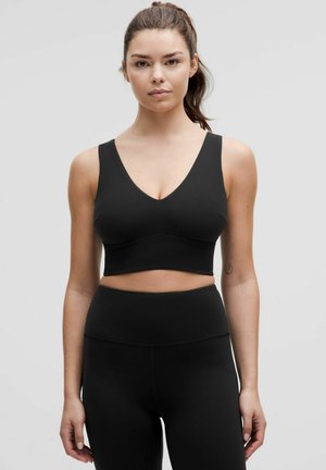 Brățară sport neagră cu un design în formă de V, curele late și o textură netedă. Asortată cu colanți negri cu talie înaltă.