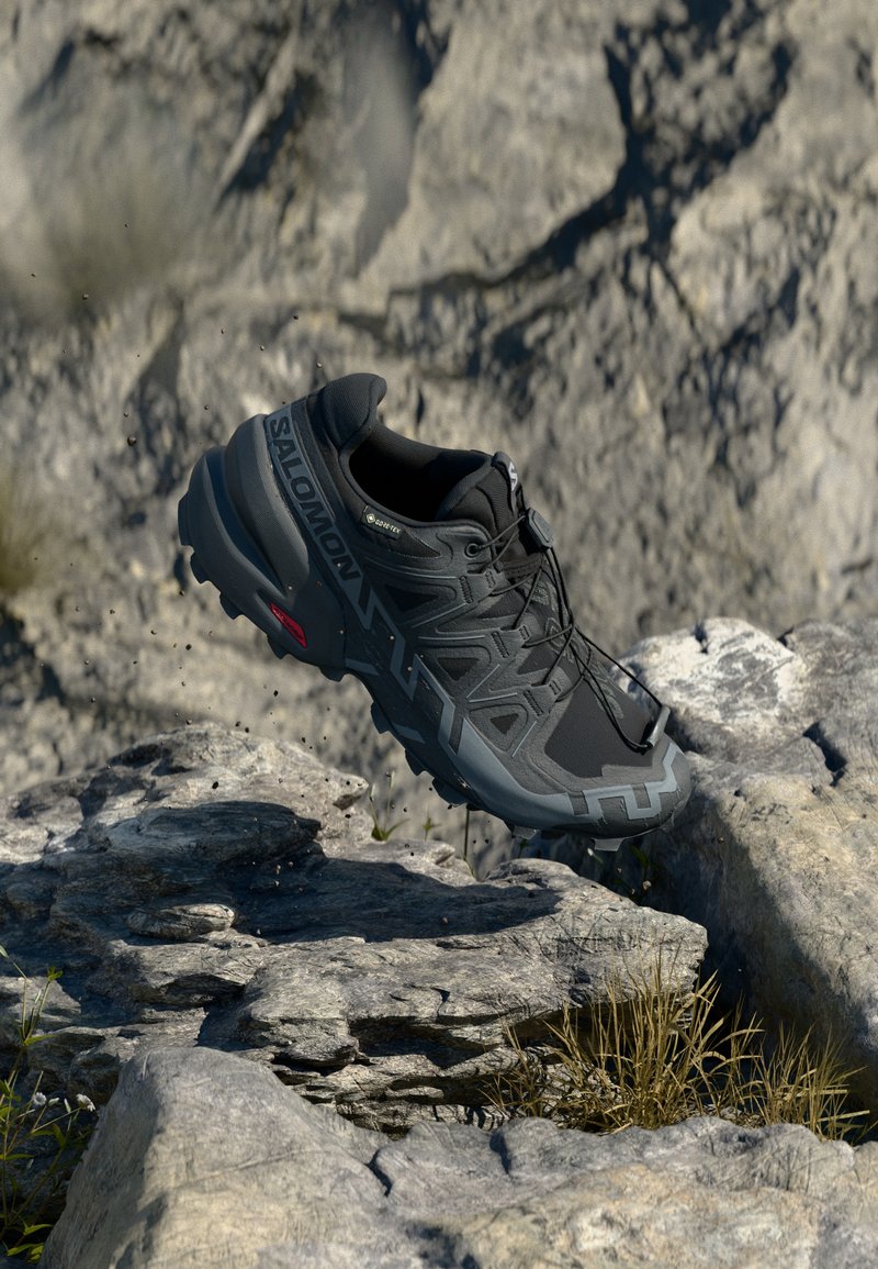 Schwarzer Sportschuh mit strukturiertem Obermaterial, robuster Sohle und verstärktem Zehenbereich, schwebend über felsigem Terrain und das elegante Design präsentierend.