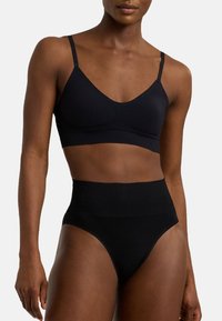 Svart bh med tunna remmar och V-ringning, kombinerad med högmidjade svarta trosor. Båda är tillverkade av glatt material utan synliga sömmar.