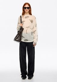 Lekki, beżowy sweter z wzorem róż, zestawiony z czarnymi szerokimi spodniami i błyszczącą, ciemnobrązową torbą typu bucket. Do kompletu dołączone czarne okulary przeciwsłoneczne.