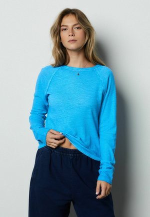 Blaues Sweatshirt mit langem Arm und Rundhalsausschnitt aus weichem Stoff, mit lockerem Sitz, kombiniert mit dunkelblauen Hosen mit elastischem Bund. Glatte Textur, ohne Muster.