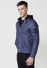 Chaqueta de cuero sintético azul con cierre delantero, acentos de hombros acanalados, dos bolsillos superiores con cremallera y detalles de rayas negras en las mangas.