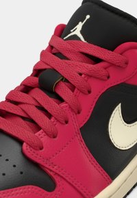 Črne in roza teniske iz usnja in sintetičnih materialov. Imajo roza vezalke, bele Nike logotipe in teksturirane črne dodatke. Poligonalna oblika.