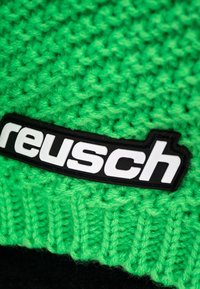 Green knitted beanie featuring a ribbed texture, highlighted by a black rectangular patch with white "reusch" lettering.
