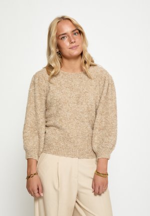 Bežani pleteni pulover s teksturiranim završetkom, okruglim izrezom i napuhanim rukavima, uparen s svijetlim naboranim hlačama.