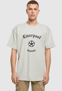 Lichtgrijze katoenen t-shirt met de tekst "Liverpool", een voetbalafbeelding en "England" eronder in zwarte letters. Korte mouwen, ontspannen pasvorm.