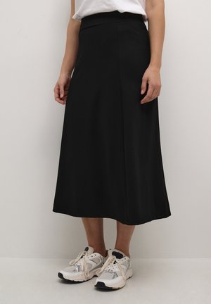 Schwarze Midirock aus glattem Stoff mit einer figurbetonten Taille und einem dezenten Seitenschlitz, kombiniert mit weißen und grauen Sportschuhen.