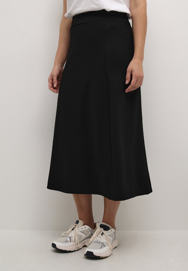 Mustat midi-hameet, jotka on valmistettu sileästä kankaasta, tiukasti istuvalla vyötäröllä ja huomaamattomalla sivuaukolla, yhdistetty valkoisiin ja harmaisiin urheilukenkä.