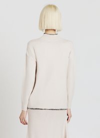 Hellbeiger Strickpullover mit hohem Kragen, geripptem Saum und langen Ärmeln. Am unteren Rand mit einem schwarzen Akzent und weicher Textur ausgestattet.