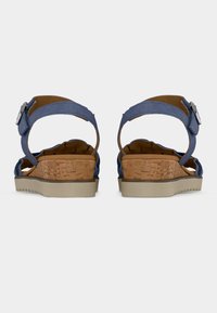 Paire de sandales bleues avec lanières à la cheville, talons compensés en liège et semelles en caoutchouc beige, vues de dos sur un fond blanc uni.