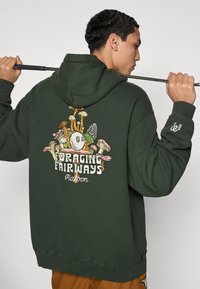 Σκούφος πράσινος με σχέδιο γραφικών από μανιτάρια και κείμενο "FORAGING FAIRWAYS" στην πλάτη. Ριμπ μανσέτες και τελείωμα, μαλακή υφή.