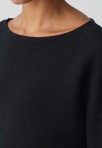 Pull noir texturé avec un col large et un tissu côtelé, présentant des lignes subtiles dans le matériau et une silhouette décontractée.