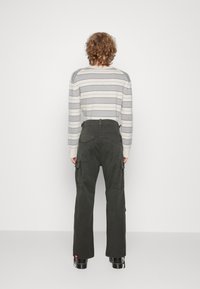 Gestreepte grijs-crème trui met een ronde halslijn, gecombineerd met donkergroene cargobroek met zijzakken en een losse pasvorm.