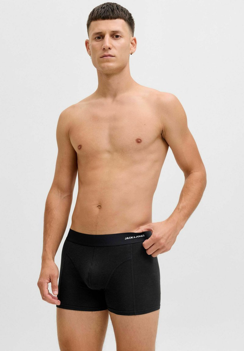 Black boxer briefs made from cotton with a soft waistband labeled "JACK & JONES"; model stands with a neutral expression against a plain background.