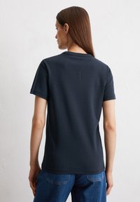 T-shirt a maniche corte blu navy realizzato in cotone morbido, con colletto rotondo e dettagli ricamati sul retro. Abbinato a jeans in denim.