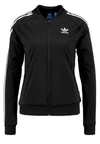 Svart zip-up jacka i slät tyg, med vita sidskarvar, ribbad mudd, två framfickor och en Adidas-logga på bröstet.