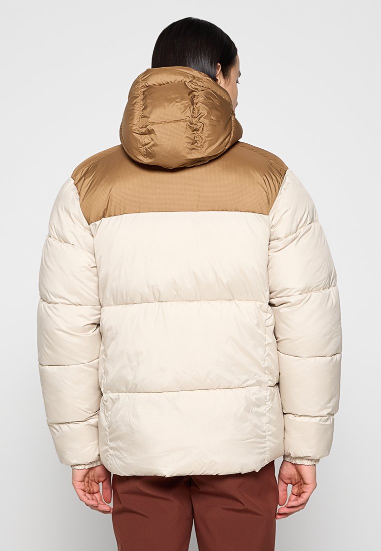 Chaqueta acolchada con sección superior marrón y sección inferior crema. Cuenta con capucha, diseño acolchado y puños elásticos. Textura sintética suave.