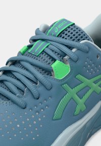 Μπλε αθλητικό παπούτσι με πράσινες λεπτομέρειες, με επάνω μέρος από δίχτυ, κυκλικά διαμπερή ανοίγματα, επίπεδους κορδόνια και υφασμένη εξωτερική σόλα για καλύτερη πρόσφυση.