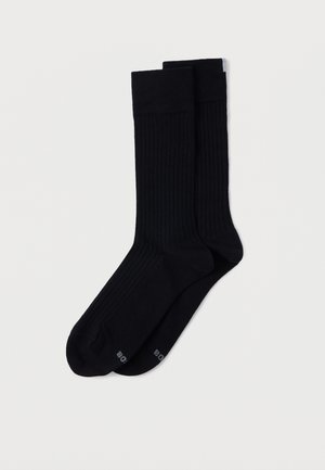 Svarta ribbade strumpor gjorda av ett stretchigt material. Har förstärkt tå och häl, med en subtil logotyp tryckt på undersidan.