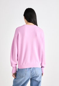 Rózsaszín, oversized pulóver bordázott mandzsettával és aljjal, kerek nyakkivágással. Világoskék, laza szabású farmernadrággal viselve.