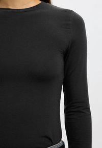 Črn dolg rokav iz gladkega materiala, z okroglim izrezom in oprijeto silhueto. Brez vidnih vzorcev ali dodatkov.