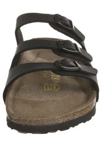 Sort lædersandal med tre justerbare stropper med metalspænder. Blødt brunt fodseng lavet af korklignende materiale. Tekstureret sål.