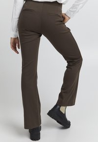 Hnedé rozšírené nohavice vyrobené z mäkkého materiálu, s prednými vreckami a spárované s čiernymi topánkami na hrubých podrážkach. Dizajn je elegantný a tesne priliehajúci.