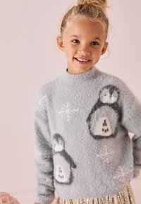 Pulli grigio chiaro e morbido con design di pinguini e fiocchi di neve. Collo alto, vestibilità ampia, texture soffice, abbinato a una gonna dorata scintillante.