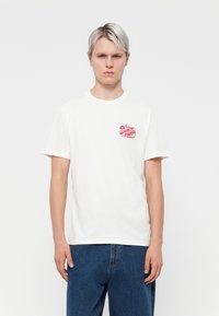 White cotton t-shirt with short sleeves, featuring a red logo print on the left chest. Straight-cut design with a classic crew neckline.