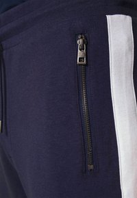 Námořnické jogger kalhoty s bílým bočním pruhem, s kapsou na zip na stehně, vyrobené z měkké, prodyšné látky, hladký povrch.