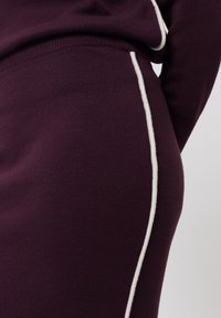 Paarse trui met een gladde textuur, voorzien van witte zijstroken en een geribde tailleband, die het aansluitende ontwerp benadrukt.