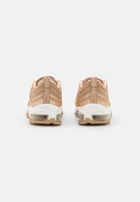 Skor: beige mesh- och lädersneakers med kurviga ränder, vit mellansula, transparent luftdämpning och en tan yttersula.