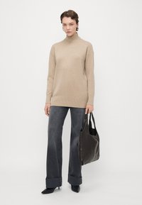 Pull à col roulé beige, long et coupe décontractée. Jean large gris foncé. Sac fourre-tout en cuir noir avec des détails brodés. Talons aiguilles noirs.