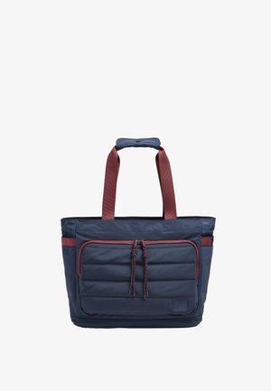 Granatowa torba na ramię z dużą przednią kieszenią na zamek, czerwonymi akcentami, wyściełanymi uchwytami i plecionymi zawieszkami zamka.