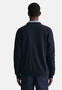 Marineblauer Strickpullover mit geripptem Saum und Bündchen. Verfügt über einen klassischen Kragen mit blauen und weißen Streifen entlang des Halsausschnitts. Einfaches Design.