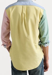 Bawełniana koszula o żółtej korpusie, jasnoniebieskim karczku oraz pastelowych różowych i zielonych rękawach. Posiada podwinięte rękawy oraz detal w postaci plisowania z tyłu.