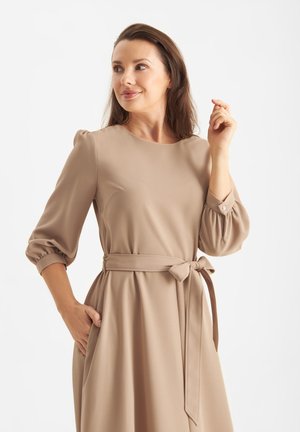 Beige jurk met driekwart pofmouwen, ronde halslijn en een strikceintuur op de taille. Gladde textuur met zijzakken.