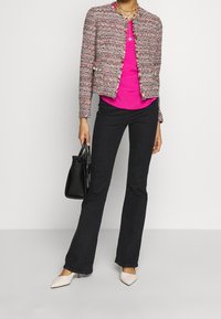 Różowy dzianinowy żakiet z teksturowanym wzorem, zestawiony z różowym topem, czarnymi rozkloszowanymi dżinsami i beżowymi szpilkami z ostrym noskiem. Akcesorium to czarna torebka.