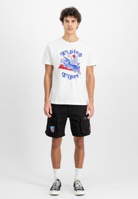 Hvid bomulds t-shirt med blå grafisk print "Flying Tiger", parret med sorte cargo-shorts med patch-lommer og broderede detaljer.