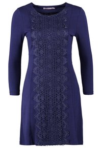 Mörkblå klänning med långärmar, med intrikata spetsdetaljer i mitten och en slät tygtextur. Figursydd silhuett.